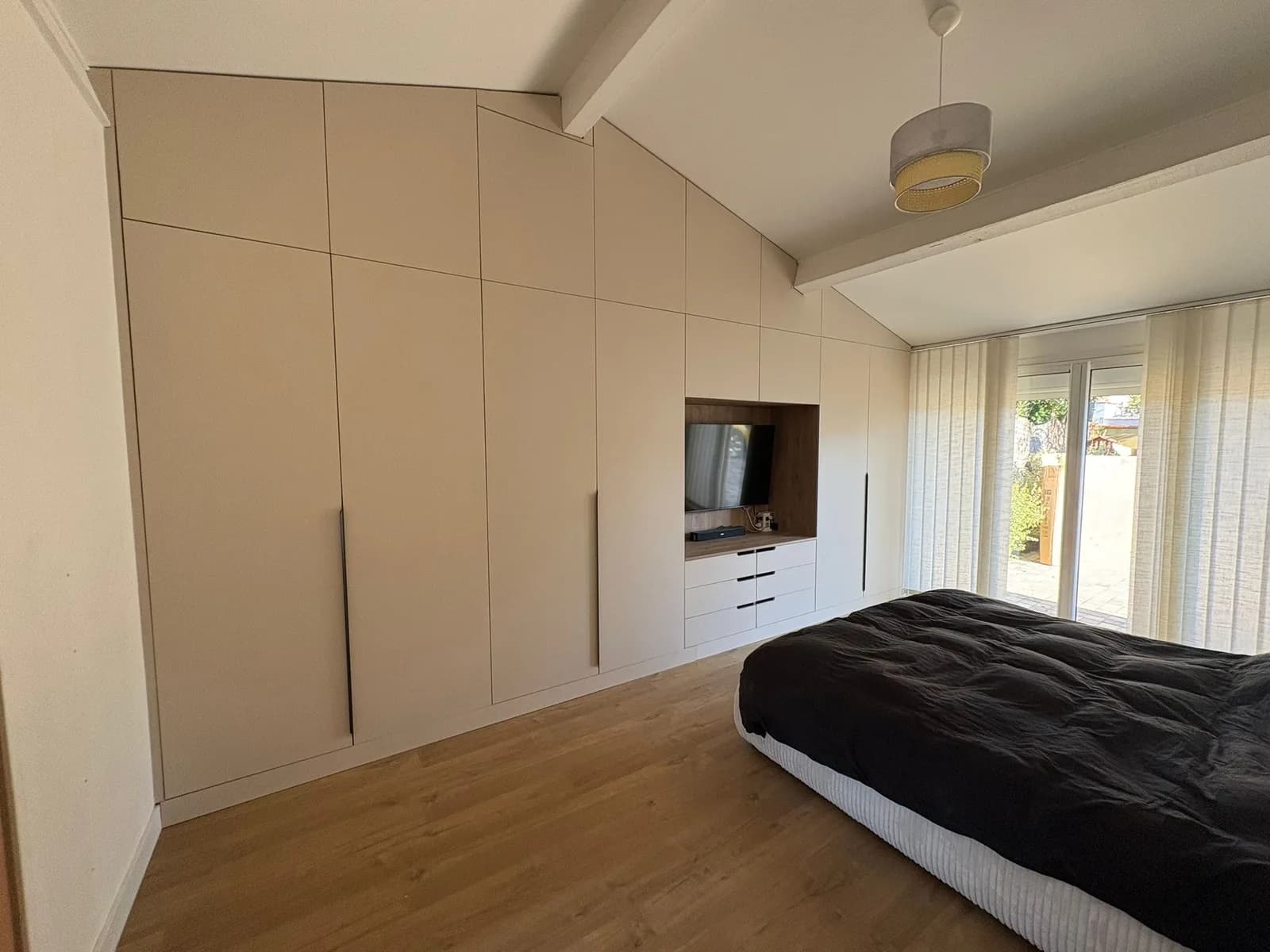Placard toute hauteur beige avec niche TV en bois et tiroirs, sous un plafond cathédrale dans une chambre