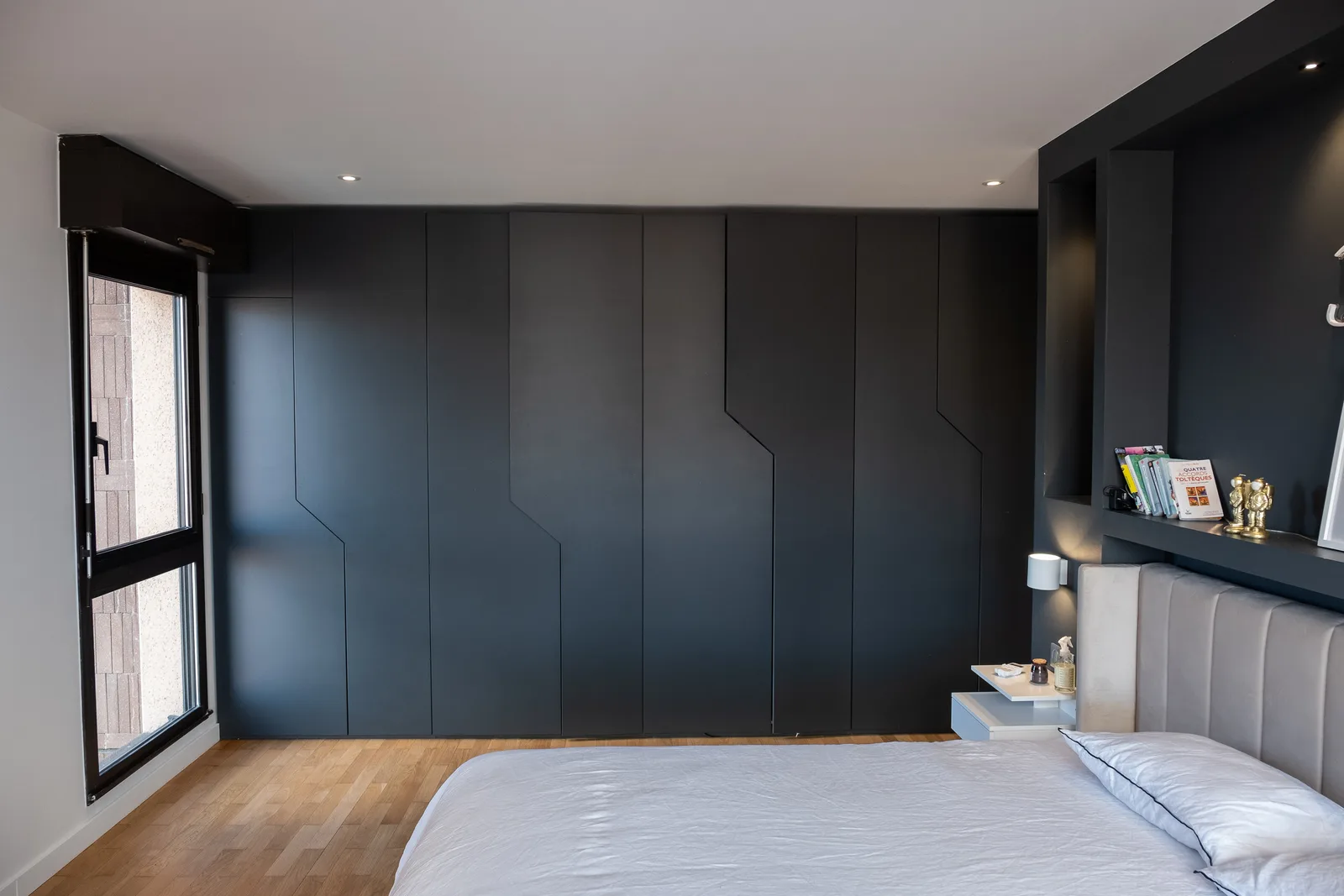 Mur de placards toute hauteur noir mat aux façades rainurées, sans poignées, dans une chambre parquetée