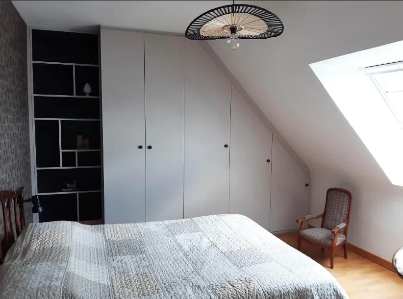 Placards gris clair suivant la pente du toit et bibliothèque noire à niches dans une chambre mansardée.